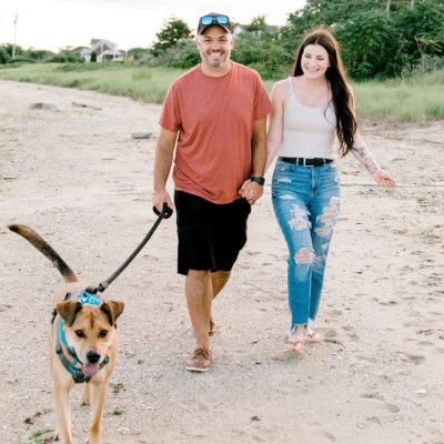 Korissa and Tom Bastianelli walking on a Rhode Island beach with their dog